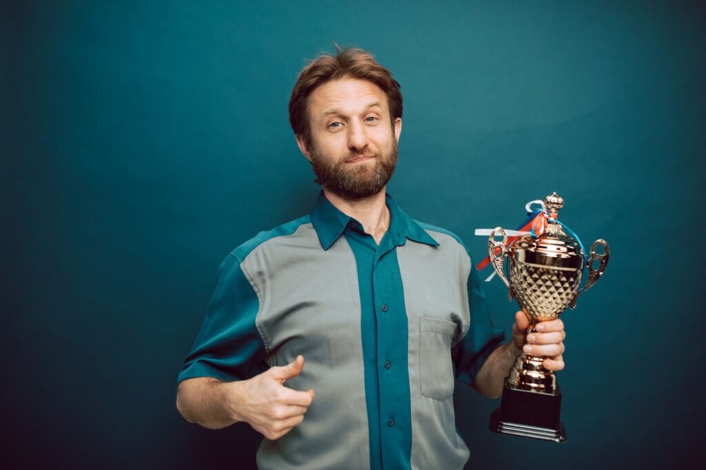 Confident man posing in studio holding a shiny trophy, showing pride in accomplishment.