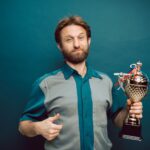 Confident man posing in studio holding a shiny trophy, showing pride in accomplishment.