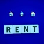 Miniature houses above letters spelling 'RENT' on a blue background, ideal for real estate themes.