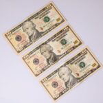 Close-up of three ten-dollar bills laid on a white surface, highlighting currency details.