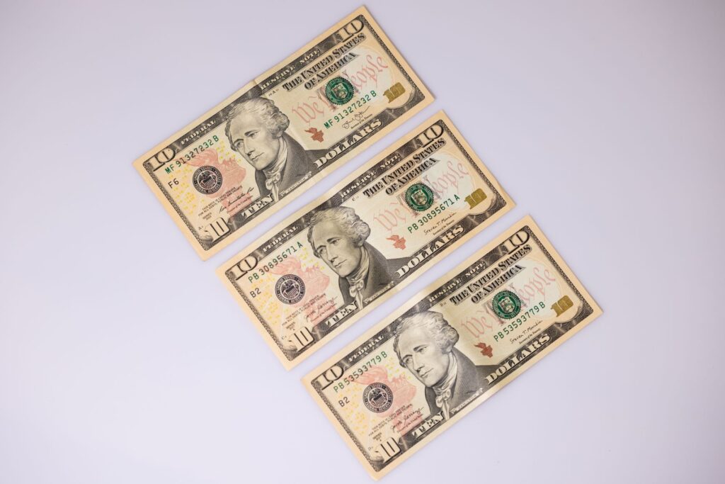 Close-up of three ten-dollar bills laid on a white surface, highlighting currency details.
