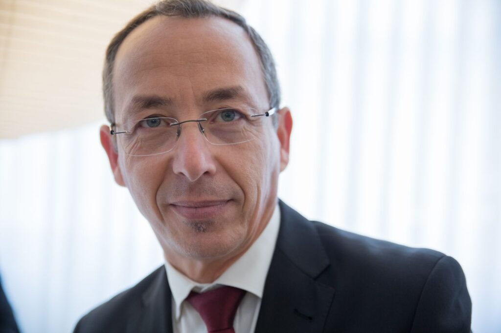 Close-up of a well-dressed businessman wearing glasses, smiling confidently indoors.