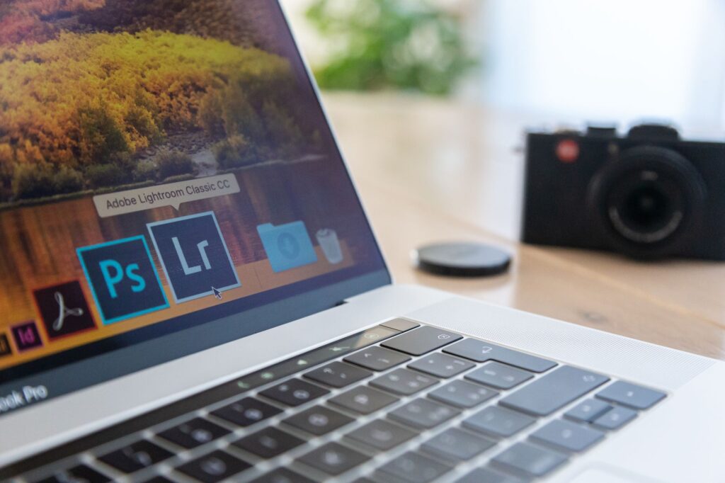 Close-up of a laptop displaying Adobe software icons, beside a camera on a desk.