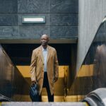 From above of mature well dressed black businessman in coat with briefcase standing on moving stairs while looking away in town