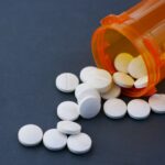 Close-up of white pills scattered from an orange prescription bottle on a gray surface.
