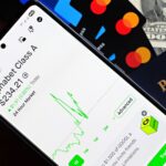 Smartphone displaying stock market app next to U.S. dollar and passport, representing global finance.