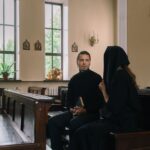 A priest discussing with a parishioner in a peaceful church setting.