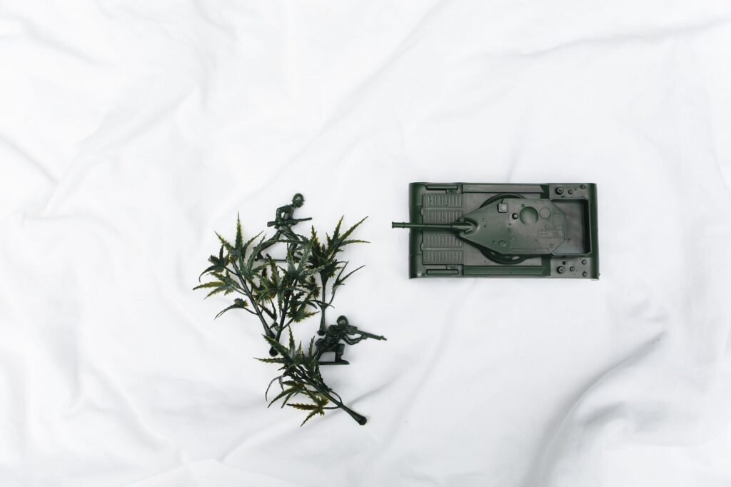 Miniature toy soldiers and tank with foliage on white fabric background.