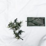 Miniature toy soldiers and tank with foliage on white fabric background.