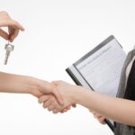 A real estate transaction with a handshake and key exchange, highlighting a home insurance document.
