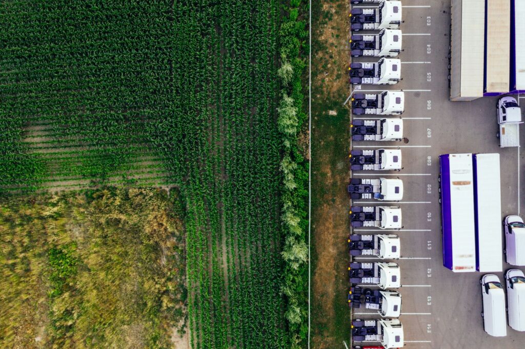 Drone shot of parked trucks next to a lush green cropland in Poznań, Poland.