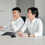 Two Asian men smiling and collaborating in a bright modern office setting.