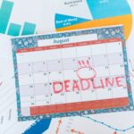 Vibrant August calendar on a desk with deadline marked in red, surrounded by graphs and charts.
