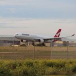 A Qantas airplane landing on a runway at Melbourne Airport during the day.
