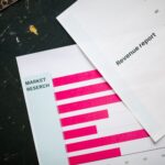Close-up of market research charts and a revenue report with a pink pen on a desk.
