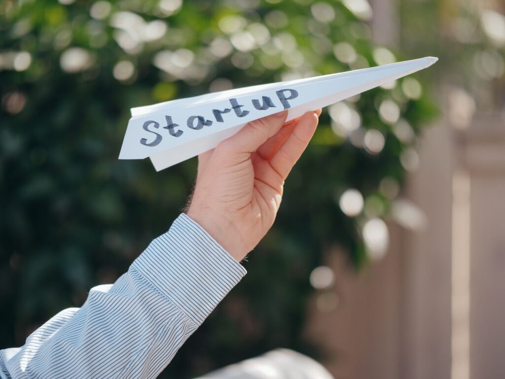 Close-up of a hand holding a paper plane with 'Startup' written, symbolizing a business launch.