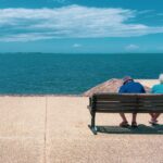 Senior couple relaxing on a seaside bench, enjoying a sunny summer day overlooking the ocean.
