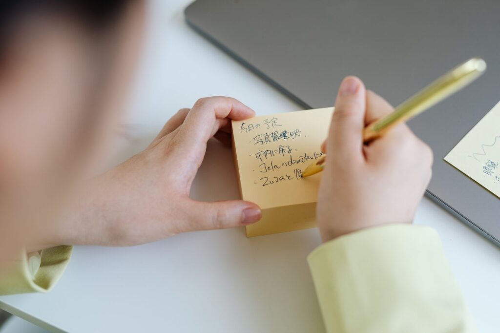 Person writing notes on sticky paper with a gold pen, taken indoors.