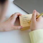 Person writing notes on sticky paper with a gold pen, taken indoors.