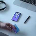 Person holding credit card by digital currency app, exploring blockchain technology.