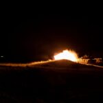 A powerful fireball eruption during nighttime military training creates a dramatic scene.
