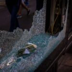 A shattered glass window on an urban street with a rose inside, capturing a moment of chaos and tranquility.