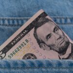 A five dollar bill tucked into a blue denim jeans pocket, symbolizing savings or cash on the go.