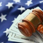 Close-up of a gavel on US dollar bills with American flag backdrop symbolizing justice and finance.