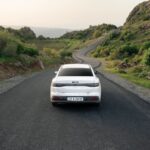 A white car travels down a winding road in the lush hills of Shaqlawa, Iraq, showcasing serene scenery.