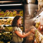 A woman selecting fresh vegetables from a supermarket aisle.