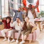 Group of friends cheering indoors with a Canadian flag, enjoying a lively moment together.