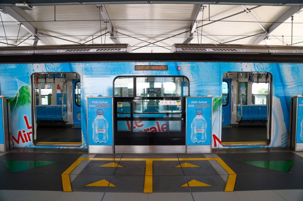 Modern metro station in Jakarta featuring a vibrant train with bold advertising graphics.