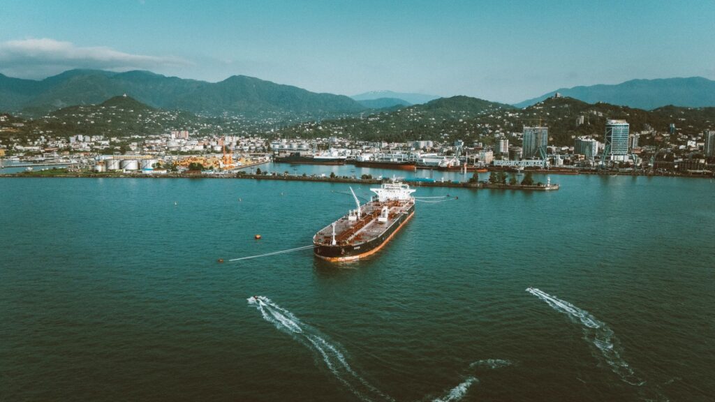 Stunning aerial view of a large ship in the port of Batumi, Georgia, surrounded by lush mountains.