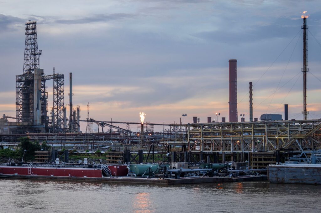 A large industrial refinery complex next to a river with a sunset backdrop.