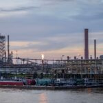 A large industrial refinery complex next to a river with a sunset backdrop.
