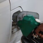 Close-up of a hand refilling a car's gas tank at a station with a green fuel nozzle.
