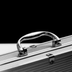 Close-up of a sturdy metal briefcase with a shiny chrome handle on a black and white background.