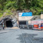 Mining entrance with tunnel BV22, rail cars, and workers in safety gear at Trinity site.
