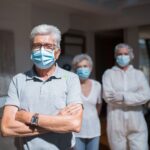Elderly couple and healthcare professional in PPE wearing face masks indoors, reflecting health precautions.