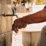 A person performing wudu, or Islamic ablution, washing hands at an outdoor tap.