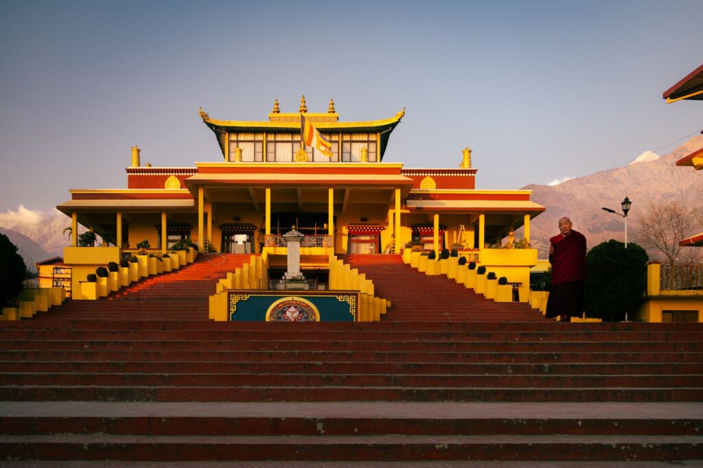 Golden sunlight illuminates a Buddhist temple in Sidhbari, with a monk standing nearby, creating a serene atmosphere.