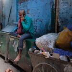 Man sitting in an urban slum using a smartphone amidst garbage and debris, New Delhi, India.
