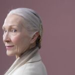 Graceful older woman posing with gray hair and subtle smile in studio setting.