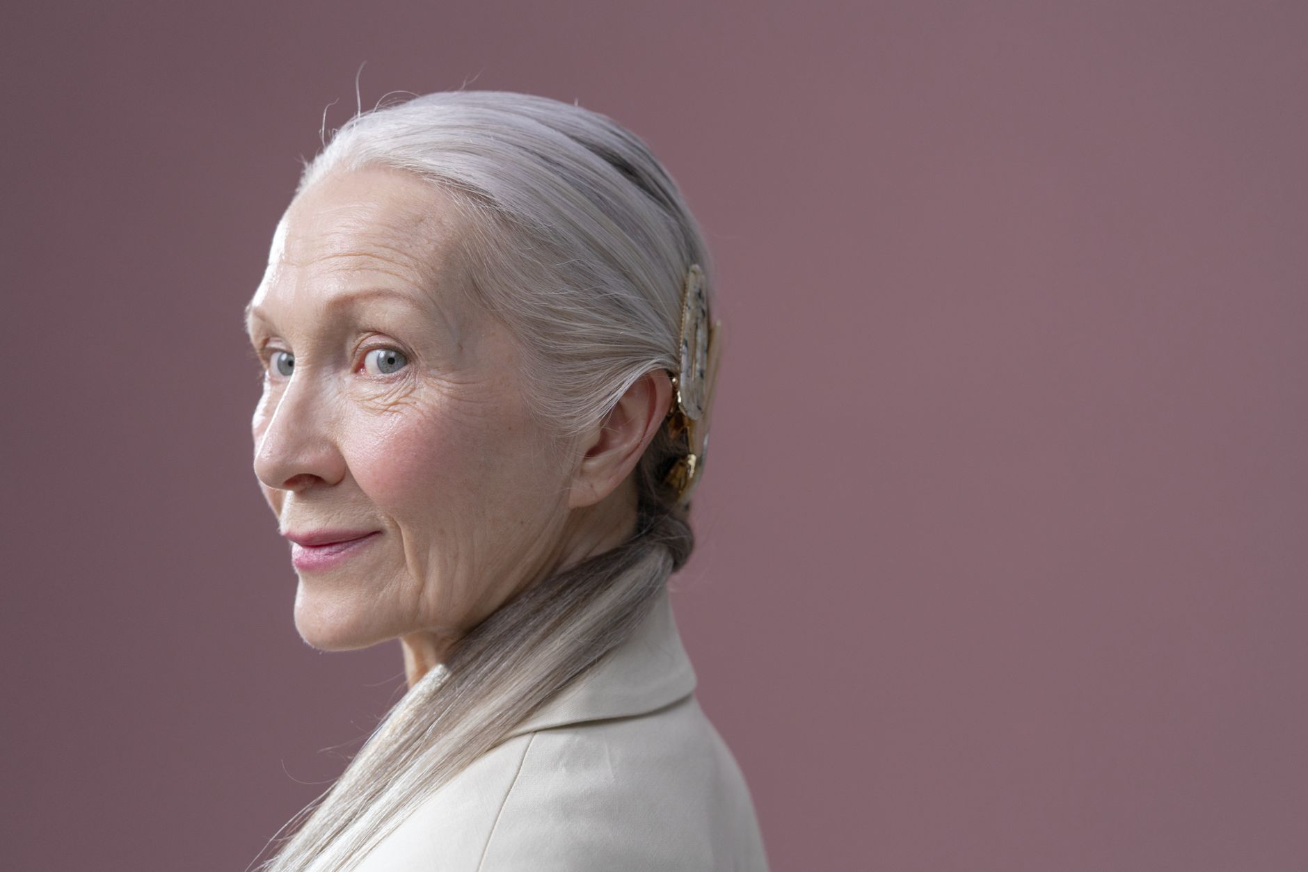 Graceful older woman posing with gray hair and subtle smile in studio setting.
