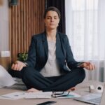 Businesswoman practicing meditation on bed in hotel room, achieving work-life balance.