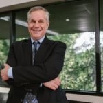 Smiling senior businessman with arms crossed standing confidently indoors.