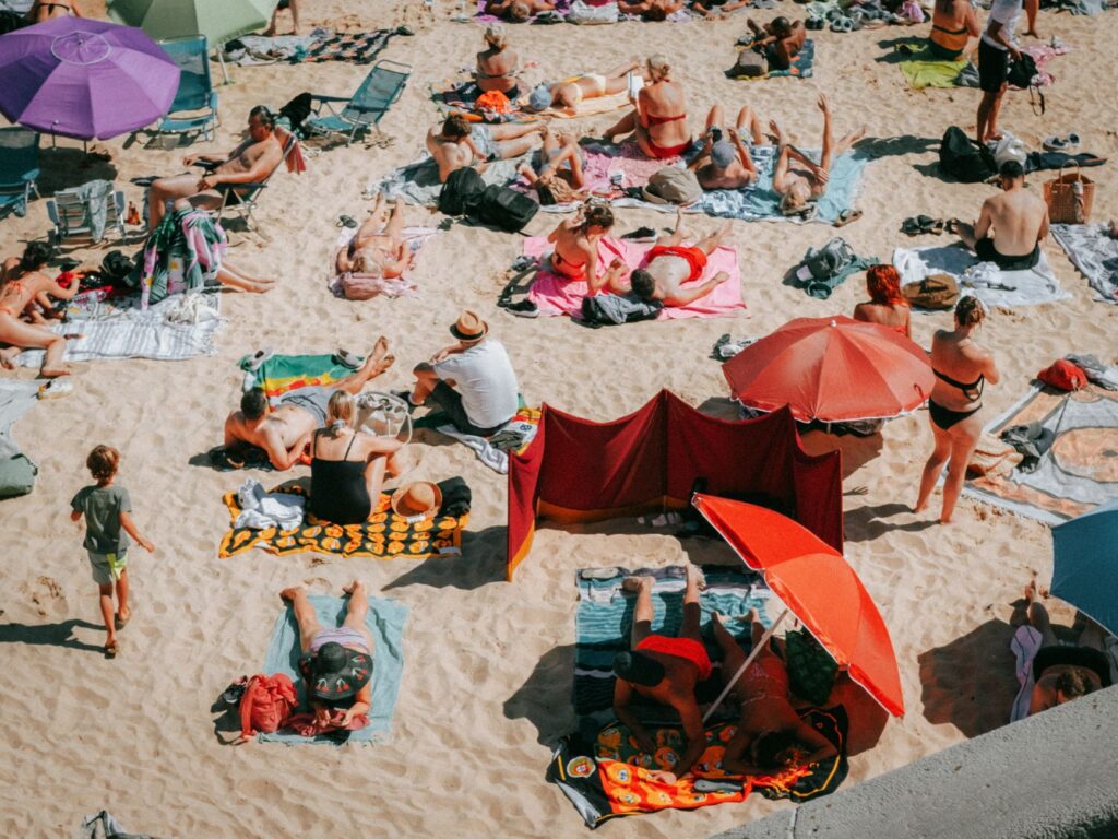 Crowded beach scene on a sunny day in Cascais, Portugal, capturing people sunbathing and enjoying leisure time.