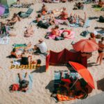 Crowded beach scene on a sunny day in Cascais, Portugal, capturing people sunbathing and enjoying leisure time.