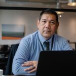 Confident ethnic male entrepreneur using laptop during business work in modern workspace and looking at camera