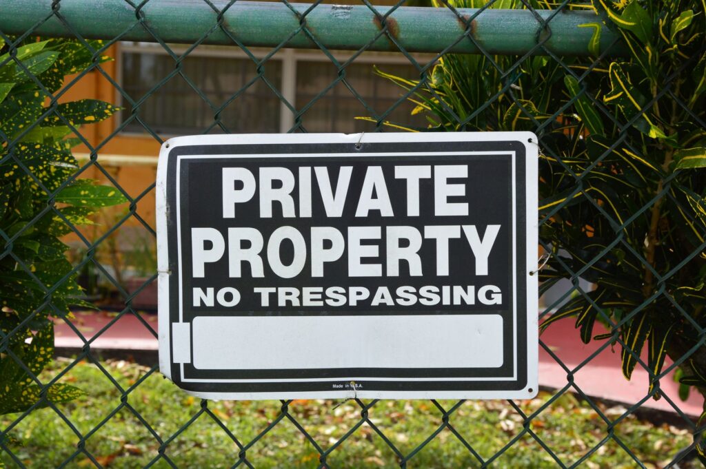 Close-up of a private property no trespassing sign on a chain-link fence with greenery in the background.